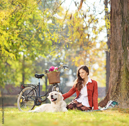 Photo: Beautiful female sitting on a green grass with her dog in a park Beautiful female sitting on a green grass with her dog in a park