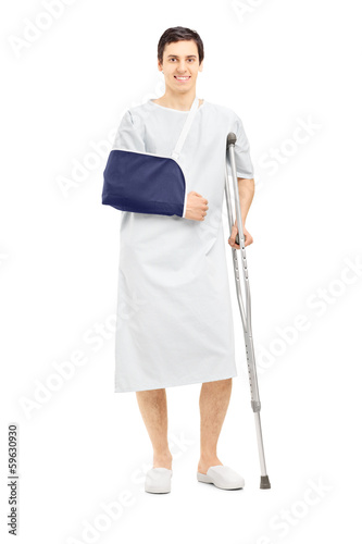 Photo: Male patient in hospital gown with broken arm holding a crutch Male patient in hospital gown with broken arm holding a crutch