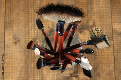 Photo: Makeup brushes in glass on wooden background Makeup brushes in glass on wooden background