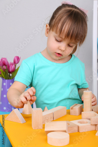 Photo: Little girl plays with construction blocks sitting at table in Little girl plays with construction blocks sitting at table in