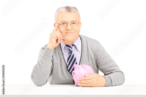 Photo: Middle aged man posing on a table with piggy bank Middle aged man posing on a table with piggy bank