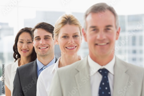 Photo: Cheerful business team standing in a line smiling at camera Cheerful business team standing in a line smiling at camera