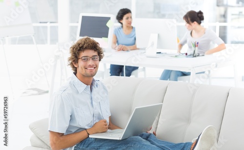 Photo: Man using laptop with colleagues at creative office Man using laptop with colleagues at creative office