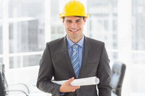 Photo: Happy architect holding blueprints smiling at camera Happy architect holding blueprints smiling at camera