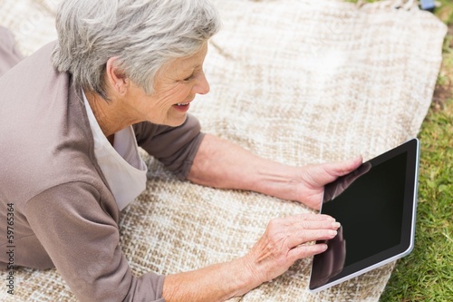 Photo: Smiling senior woman using digital tablet at park Smiling senior woman using digital tablet at park