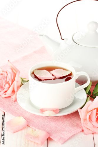 Photo: teapot and cup of tea with roses and on white wooden table teapot and cup of tea with roses and on white wooden table