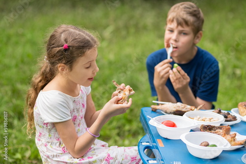 Photo: Boy and girl eat meat with vegetables at the picnic Boy and girl eat meat with vegetables at the picnic