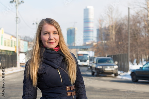 Photo: girl in warm clothes on street on background of skyscrapers girl in warm clothes on street on background of skyscrapers