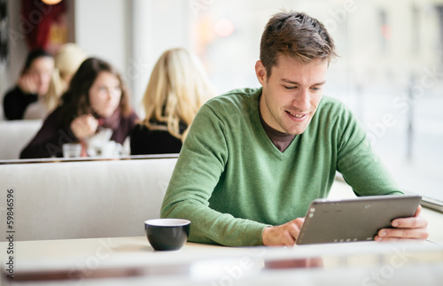 Photo: Young man / student using tablet computer in cafe Young man / student using tablet computer in cafe