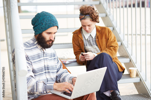 Photo: Hipster couple using computer and smartphone outdoors Hipster couple using computer and smartphone outdoors