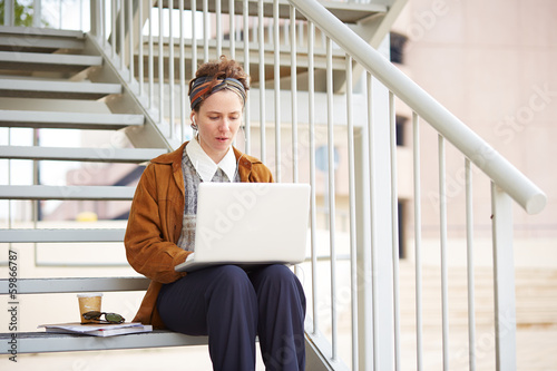 Photo: Young redhead hipster woman student using computer outdoors Young redhead hipster woman student using computer outdoors