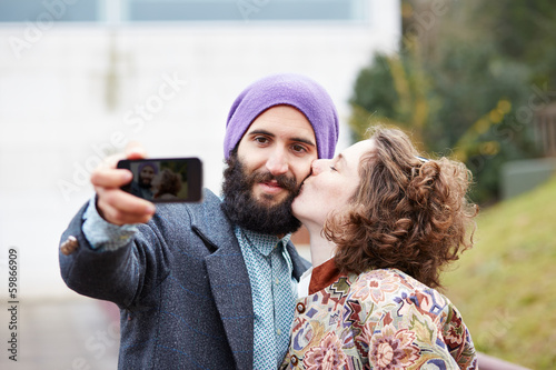 Photo: Couple taking a photograph of themselves kissing with a smartpho Couple taking a photograph of themselves kissing with a smartpho