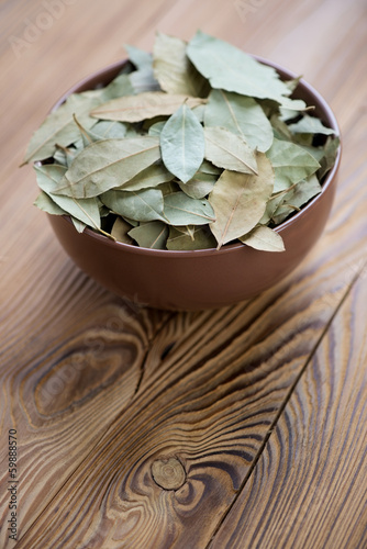 Photo: Bowl with dried bay leaves on a wooden table, vertical shot Bowl with dried bay leaves on a wooden table, vertical shot