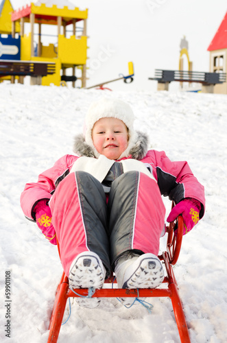 Photo: Pretty little girl playing on a sled in the snow Pretty little girl playing on a sled in the snow