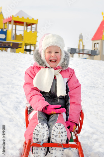 Photo: Pretty little girl playing on a sled in the snow Pretty little girl playing on a sled in the snow