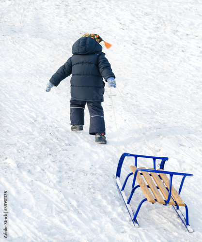 Photo: Little child pulling a blue sled on the snow Little child pulling a blue sled on the snow