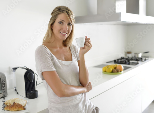 Photo: Cheerful young woman having coffee in kitchen Cheerful young woman having coffee in kitchen