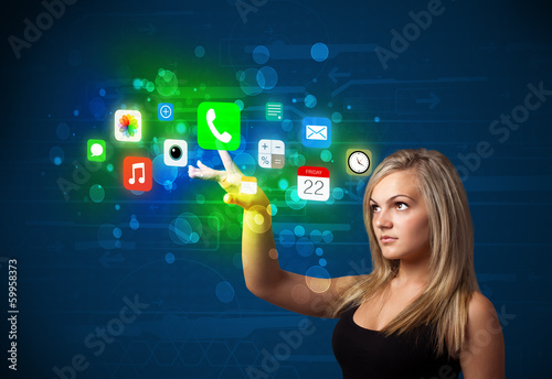 Photo: Young businesswoman pressing colorful mobile app icons with boke Young businesswoman pressing colorful mobile app icons with boke