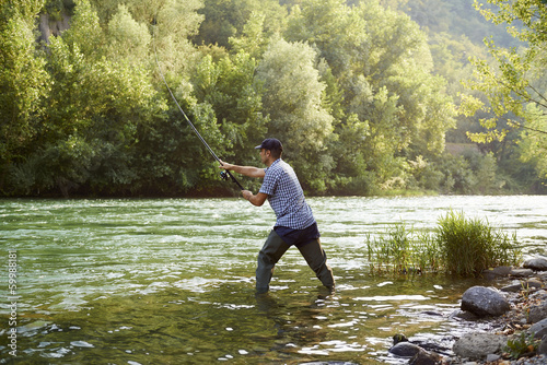 Photo: Fisherman standing near river and holding fishing rod Fisherman standing near river and holding fishing rod