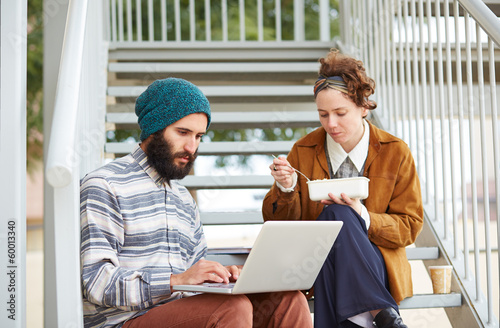 Photo: Hipster couple using computer and eating lunch outdoors Hipster couple using computer and eating lunch outdoors