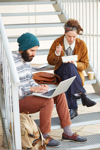Photo: Hipster couple using computer and eating lunch outdoors Hipster couple using computer and eating lunch outdoors