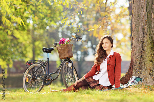 Photo: Beautiful female with bicycle sitting in a park and looking at c Beautiful female with bicycle sitting in a park and looking at c