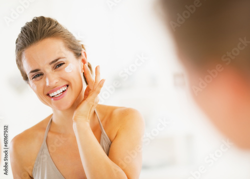 Photo: Happy young woman applying cream in bathroom Happy young woman applying cream in bathroom