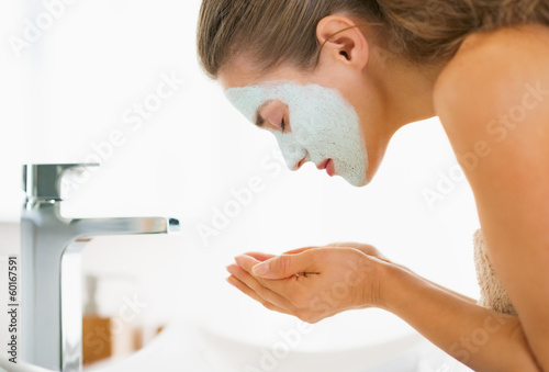 Photo: Young woman with cosmetic mask on face washing Young woman with cosmetic mask on face washing