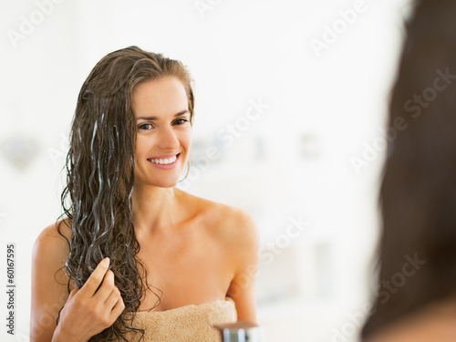 Photo: Happy young woman applying hair mask in bathroom Happy young woman applying hair mask in bathroom