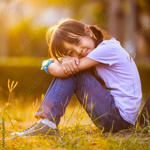 Photo: Happy girl sitting on grass in garden Happy girl sitting on grass in garden