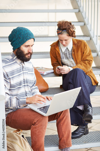 Photo: Hipster couple using computer and smartphone outdoors Hipster couple using computer and smartphone outdoors