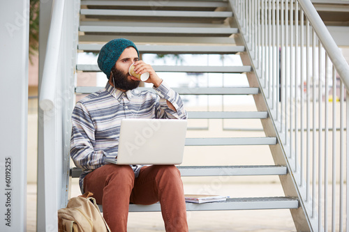 Photo: Young bearded hipster student using computer outdoors Young bearded hipster student using computer outdoors