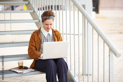 Photo: Young redhead hipster woman student using computer outdoors Young redhead hipster woman student using computer outdoors