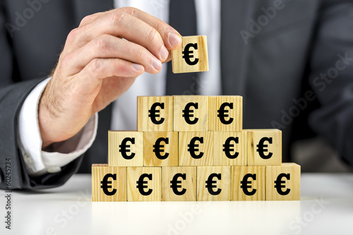 Photo: Man building a pyramid of euro symbols Man building a pyramid of euro symbols