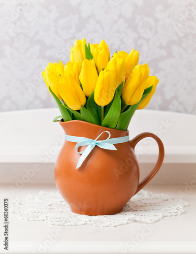 Photo: yellow tulips in vase with blue bow on white table yellow tulips in vase with blue bow on white table
