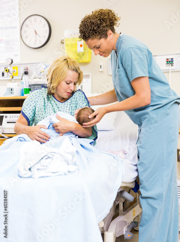 Photo: Nurse Helping Woman In Holding Newborn Baby At Hospital Nurse Helping Woman In Holding Newborn Baby At Hospital