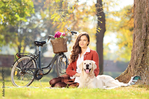 Photo: Beautiful female sitting on a grass with her dog in a park Beautiful female sitting on a grass with her dog in a park