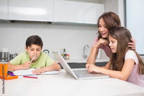 Photo: Mother with kids using laptop in kitchen Mother with kids using laptop in kitchen