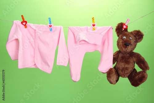 Photo: Baby clothes hanging on clothesline, on color background Baby clothes hanging on clothesline, on color background