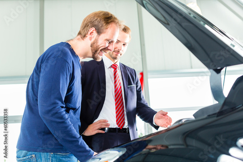 Photo: Young man and seller with auto in car dealership Young man and seller with auto in car dealership
