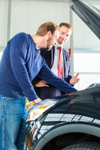 Photo: Young man and seller with auto in car dealership Young man and seller with auto in car dealership