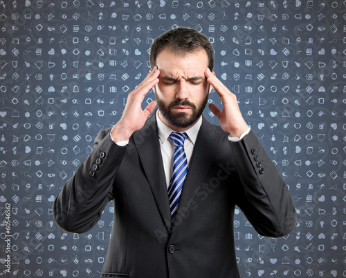 Photo: Young businessman with headache over blue background with icons Young businessman with headache over blue background with icons