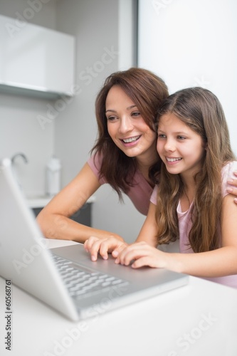 Photo: Smiling mother with daughter using laptop in kitchen Smiling mother with daughter using laptop in kitchen