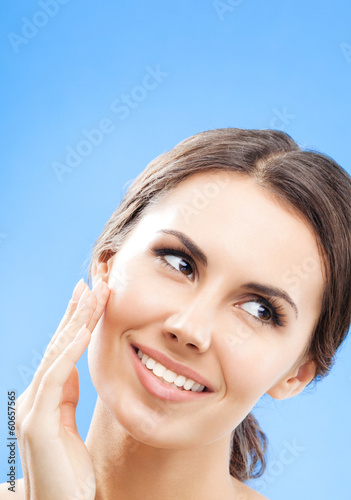 Photo: Woman touching skin or applying cream, over blue Woman touching skin or applying cream, over blue
