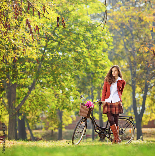 Photo: Beautiful young woman posing in park with her bicycle Beautiful young woman posing in park with her bicycle