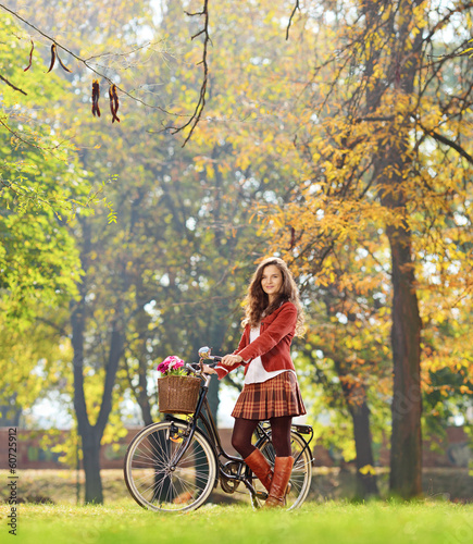 Photo: Smiling young female standing with bicycle in park Smiling young female standing with bicycle in park
