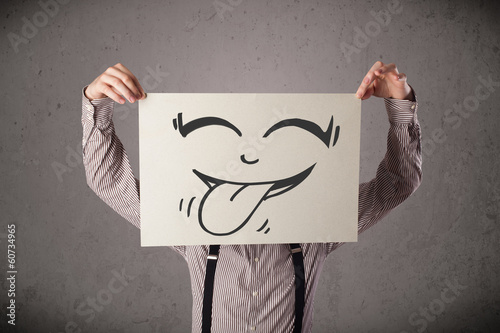 Photo: Businessman holding a paper with funny smiley face in front of h Businessman holding a paper with funny smiley face in front of h