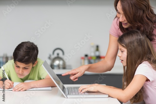 Photo: Mother with kids using laptop in kitchen Mother with kids using laptop in kitchen