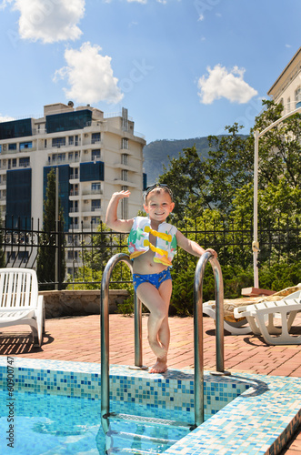 Photo: Happy little boy waving at the camera poolside Happy little boy waving at the camera poolside
