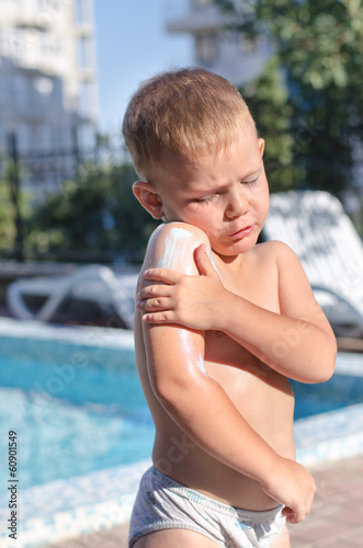 Photo: Little boy applying suntan lotion to his skin Little boy applying suntan lotion to his skin